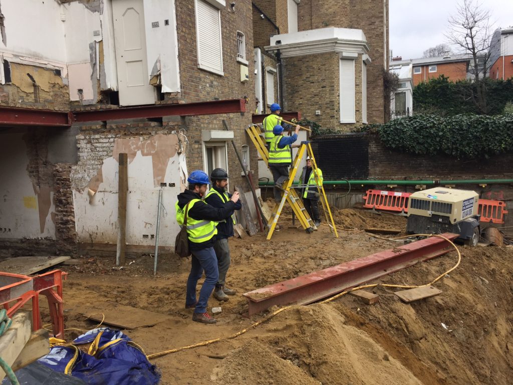 Construction team working alongside the exposed rear wall of the property — a critical phase requiring precise underpinning to maintain structural integrity.
